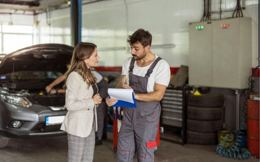 A woman talking to a mechanic at a service station.